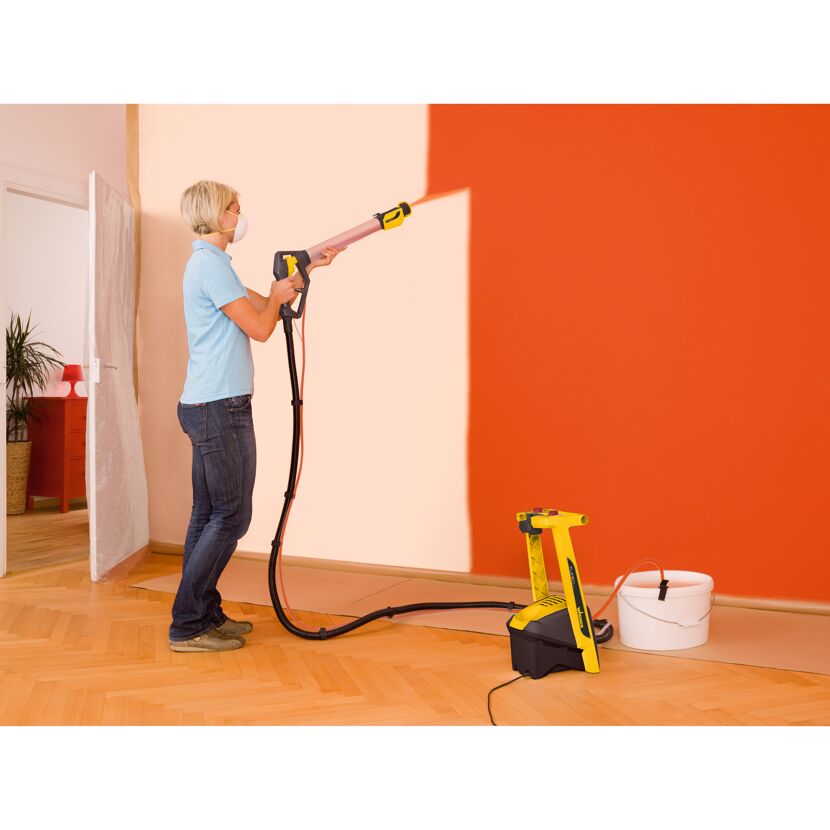 Person streicht eine Wand mit einem Farbsprühsystem orange.