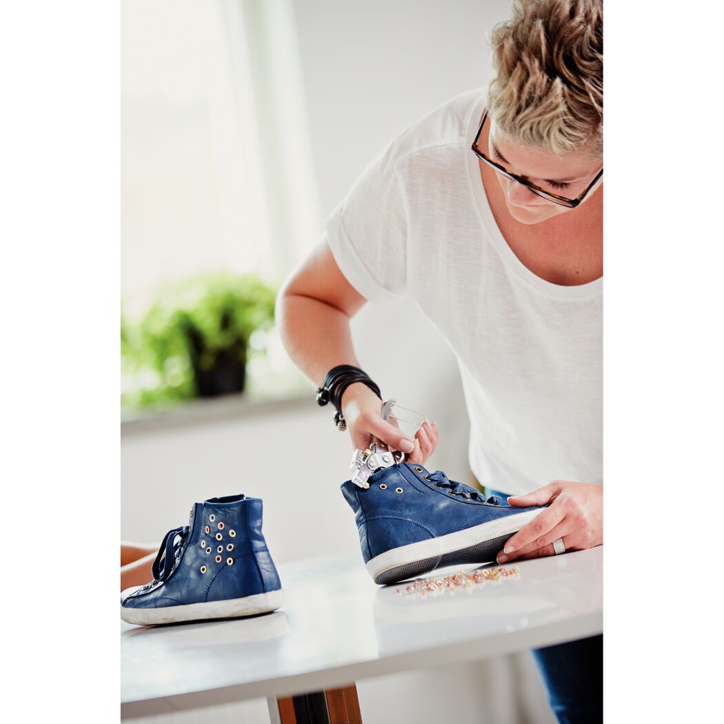 Person befestigt Ösen an einem Schuh mit einer Ösenzange.