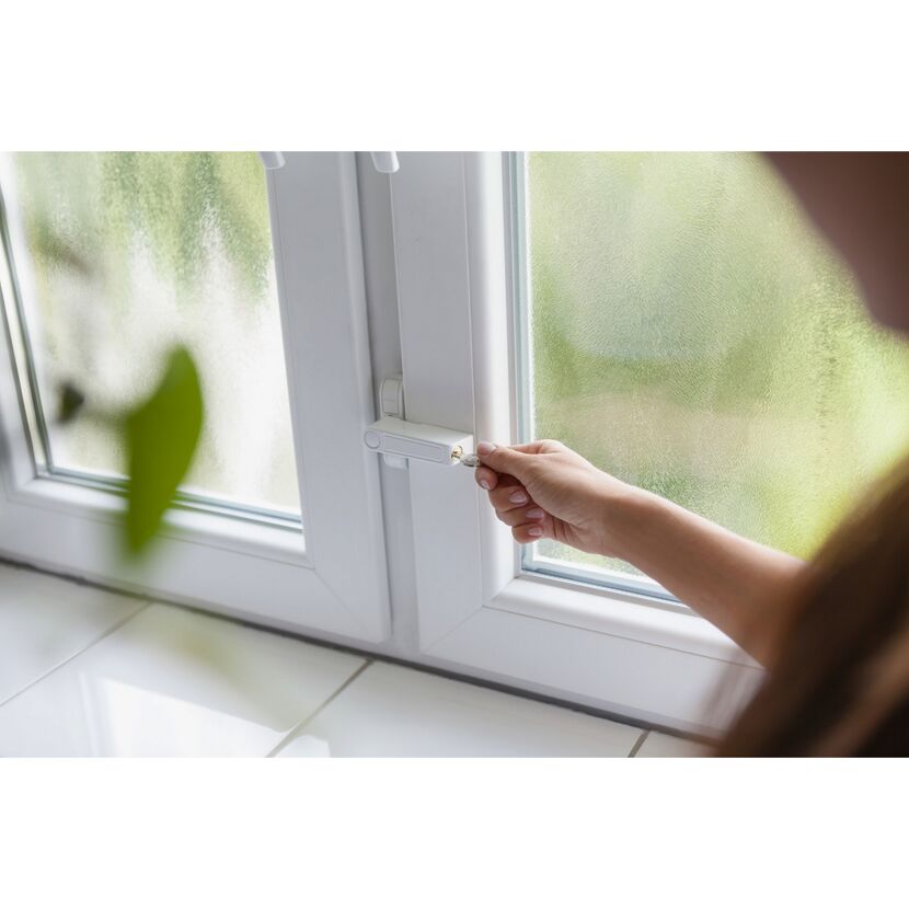 Person verschließt ein Fenster mit einem Schlüssel.