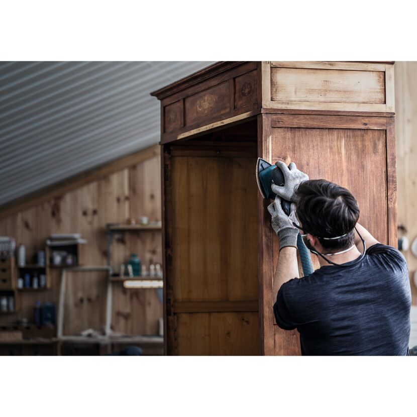 Person schleift einen alten Schrank mit einem Schwingschleifer