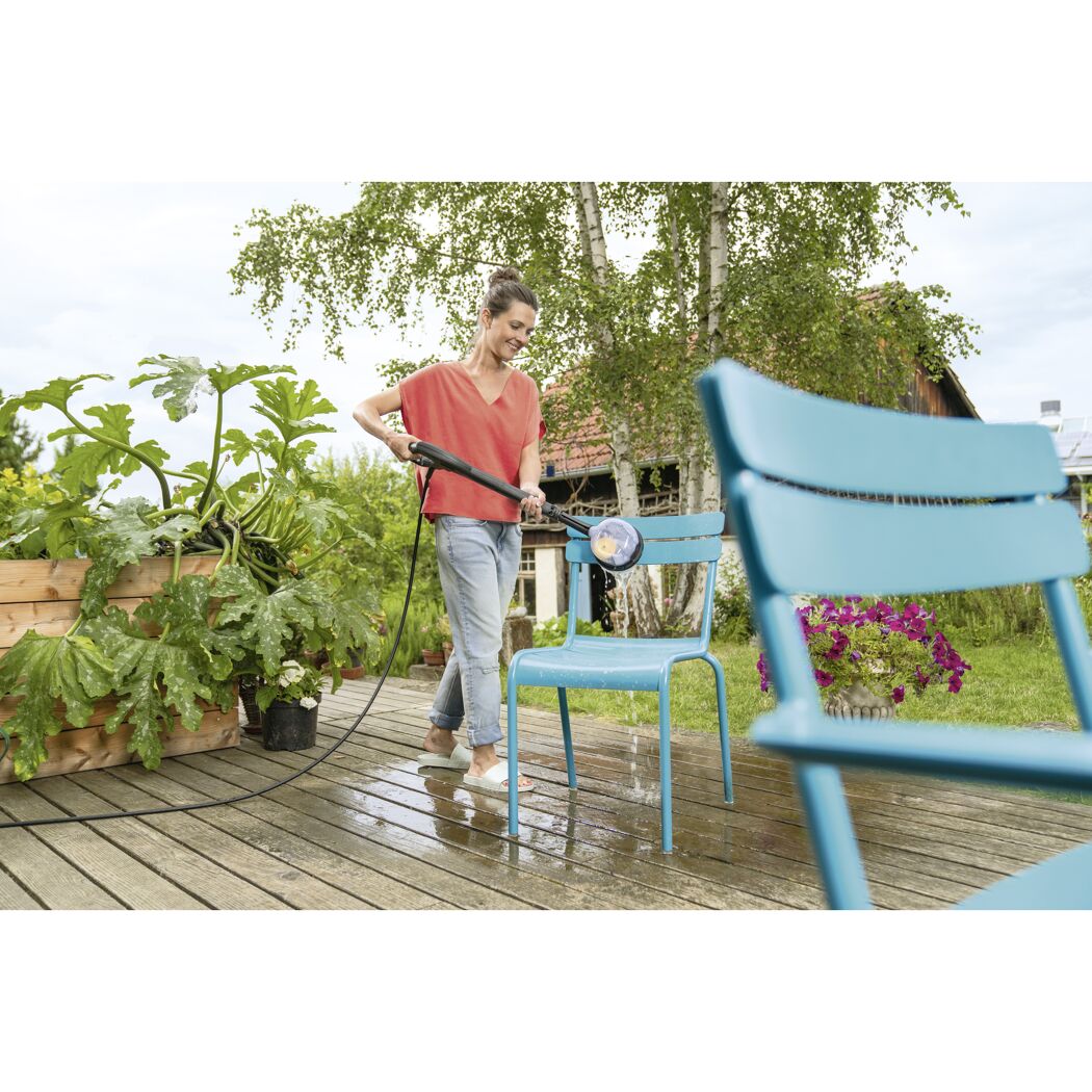 Person reinigt einen blauen Gartenstuhl mit einer Waschbürste.