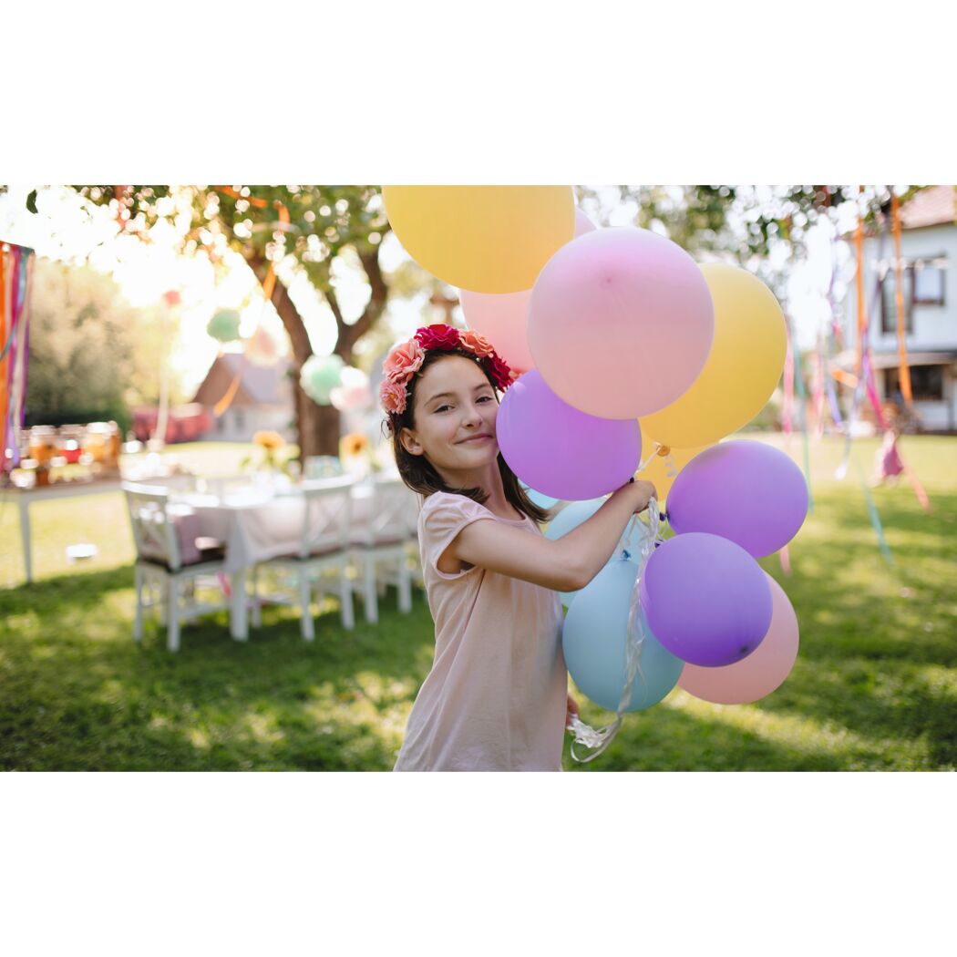 Kind mit Blumenkranz hält bunte Luftballons
