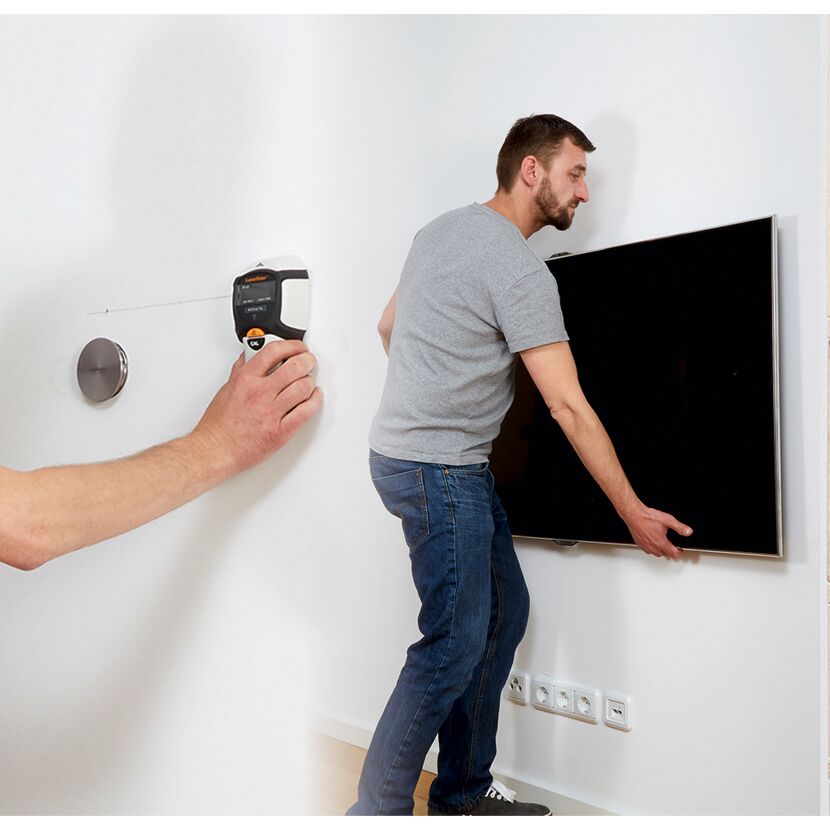 Person bringt mit Detektor und Wasserwaage Fernseher an