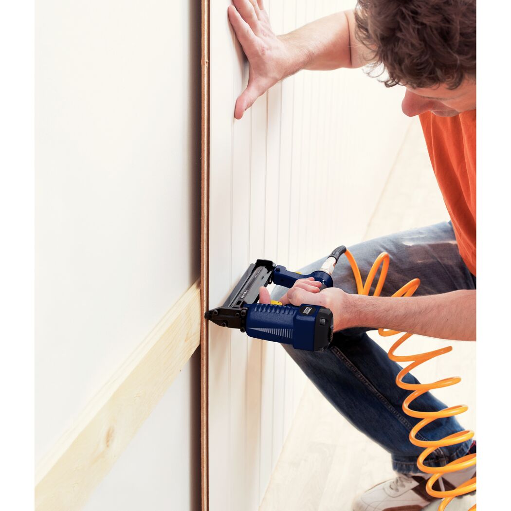 Person befestigt Holzpaneel mit Drucklufttacker an Wand.