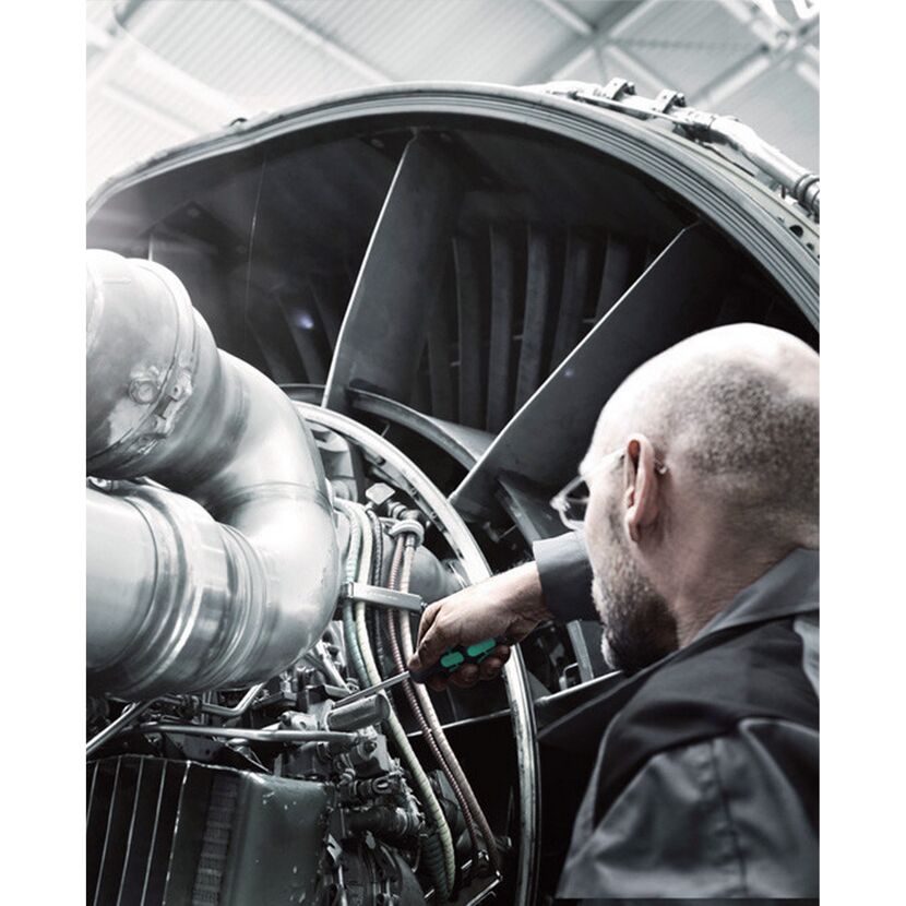 Person repariert ein Flugzeugtriebwerk mit einem Schraubendreher.