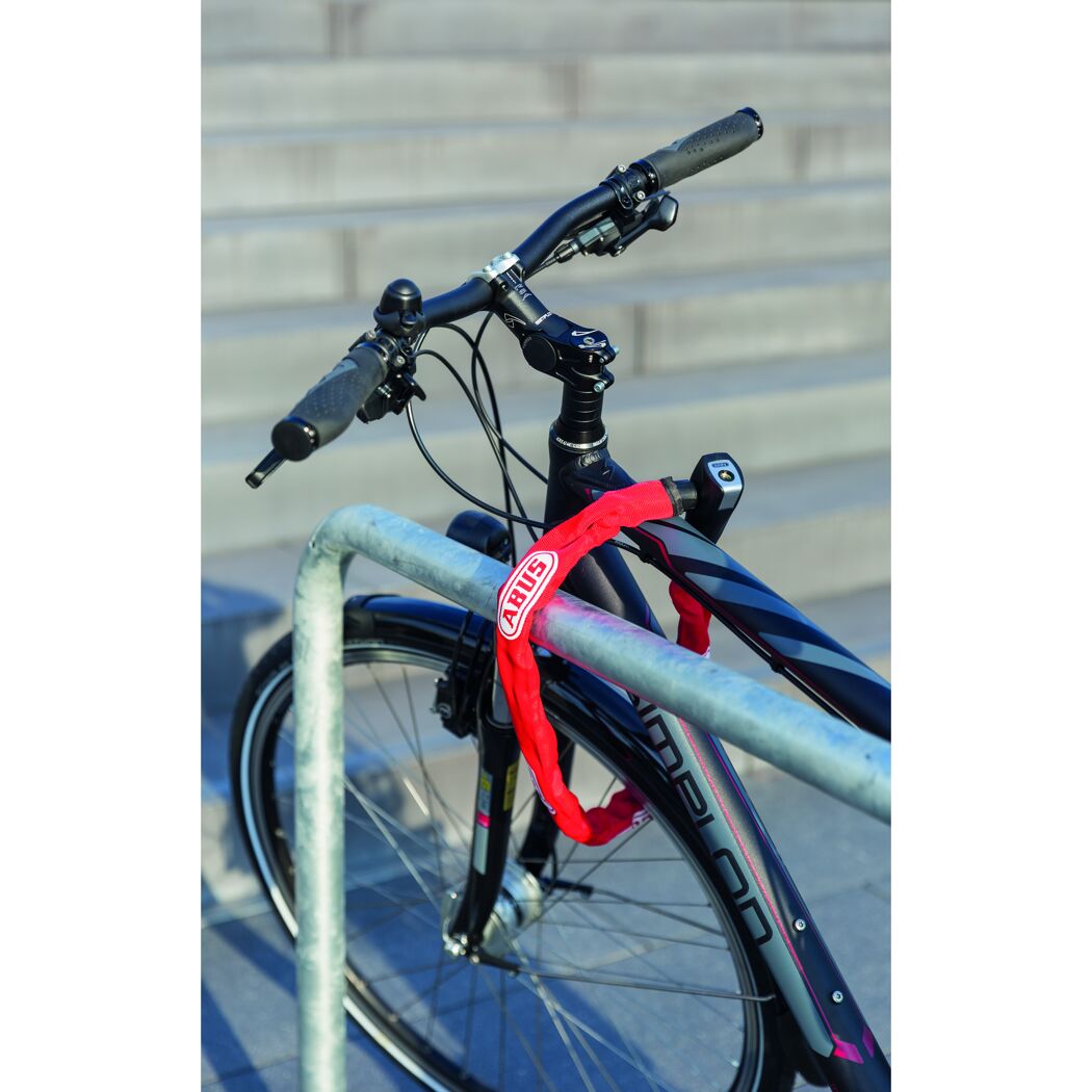 Fahrrad mit rotem Kettenschloss an einem Metallgeländer angeschlossen.