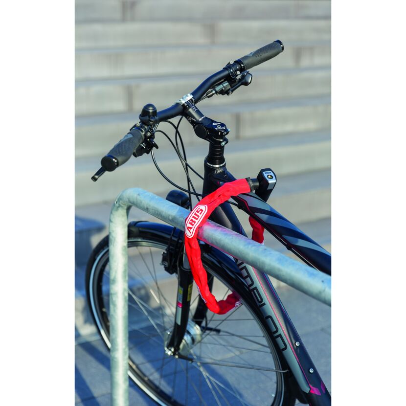 Fahrrad mit rotem Kettenschloss an einem Metallgeländer angeschlossen.