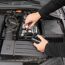 Person schließt ein Batterieladegerät an eine Autobatterie an.