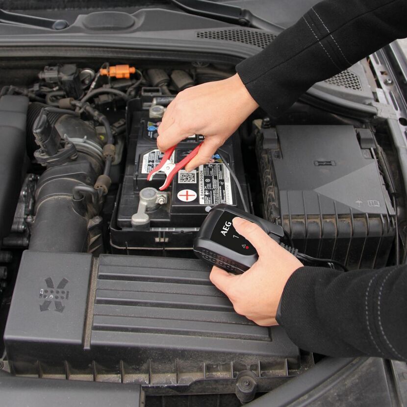 Person schließt ein Batterieladegerät an eine Autobatterie an.