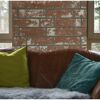 Ledersofa mit grünen und türkisen Kissen vor Ziegelwand
