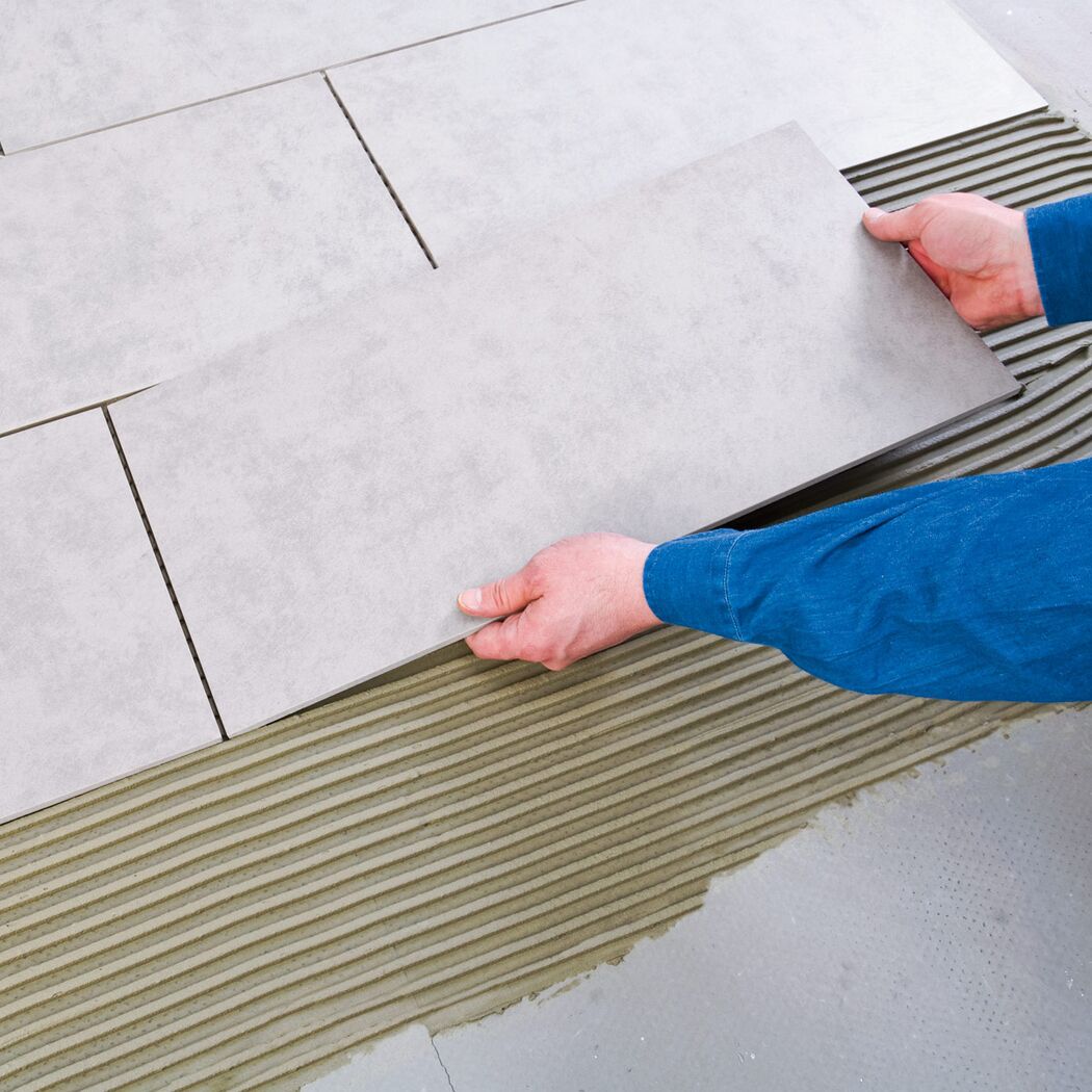 Person verlegt graue Bodenfliesen mit Flexkleber