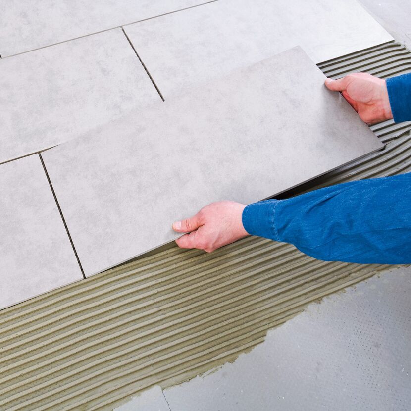 Person verlegt graue Bodenfliesen mit Flexkleber