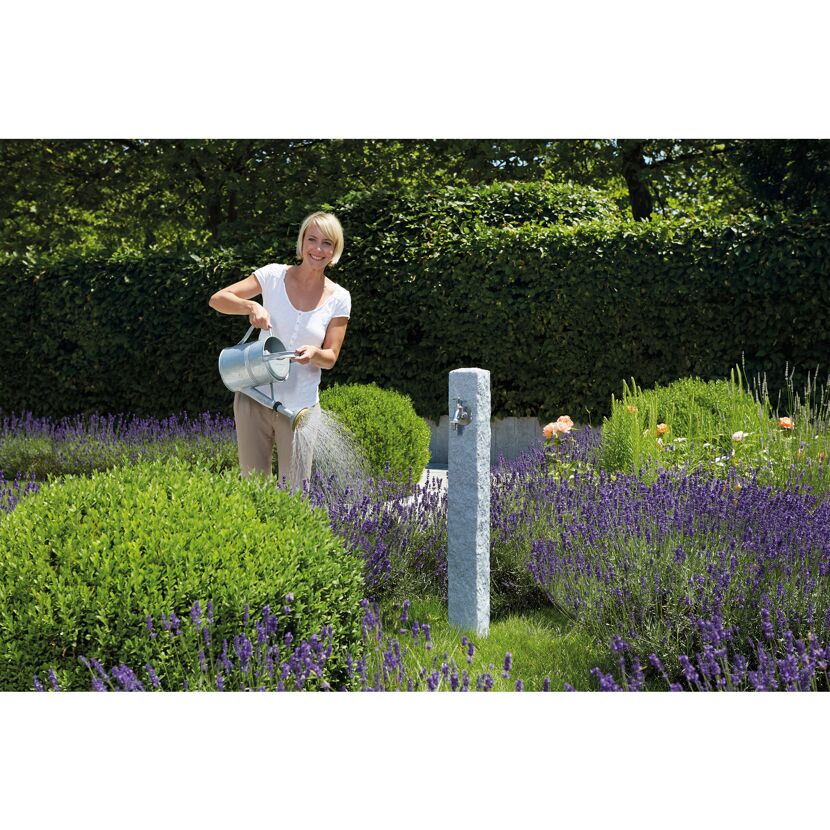 Person gießt mit Gießkanne Pflanzen im Garten.