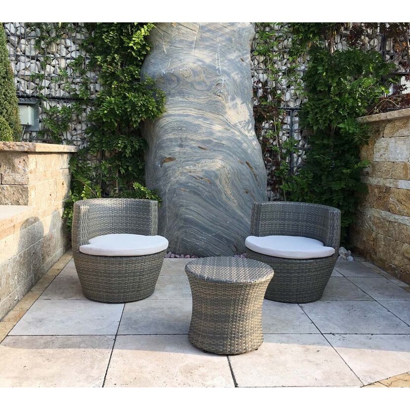 Zwei graue Gartenstühle mit weißem Sitzkissen und ein grauer Tisch auf hellen Fliesen.