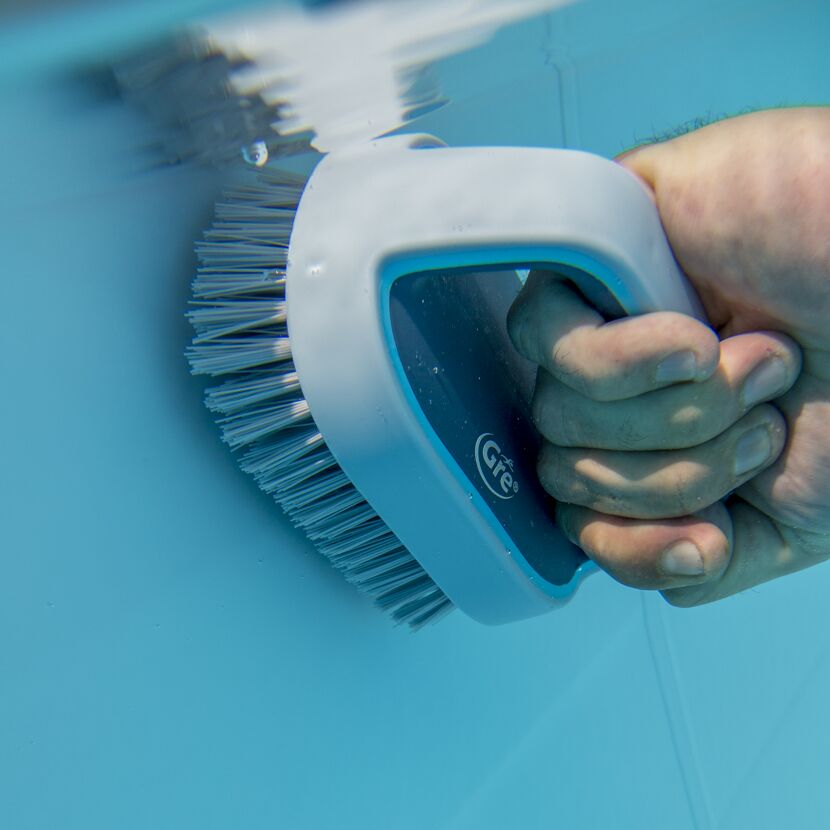 Person reinigt einen Pool mit einer Bürste.