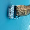Hand reinigt blauen Pool mit Bürste