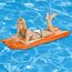 Person liegt auf einer orangen Luftmatratze im Pool
