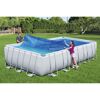 Zwei Personen decken einen rechteckigen Pool mit einer blauen Solar-Poolabdeckung ab.