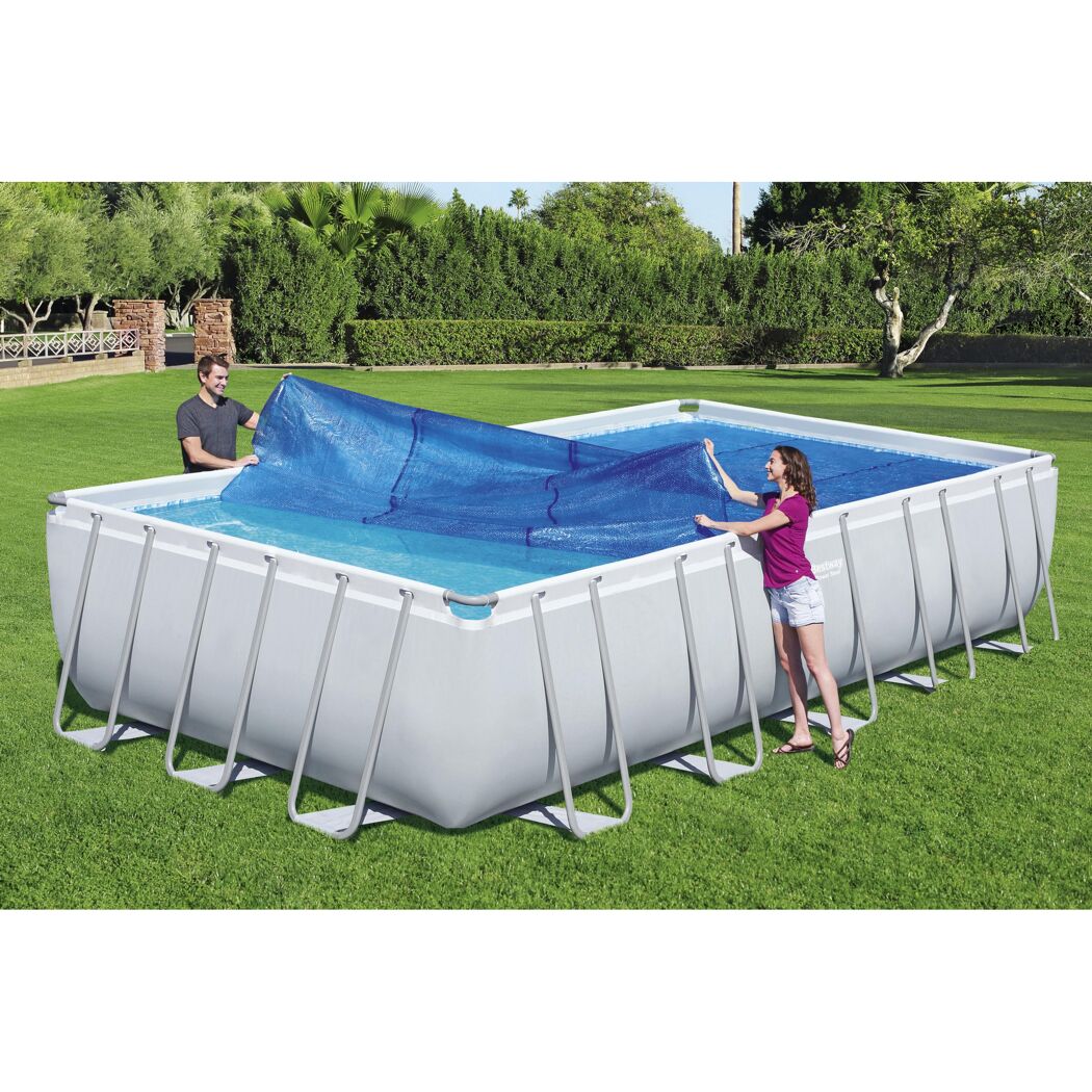 Zwei Personen decken einen rechteckigen Pool mit einer blauen Solar-Poolabdeckung ab.