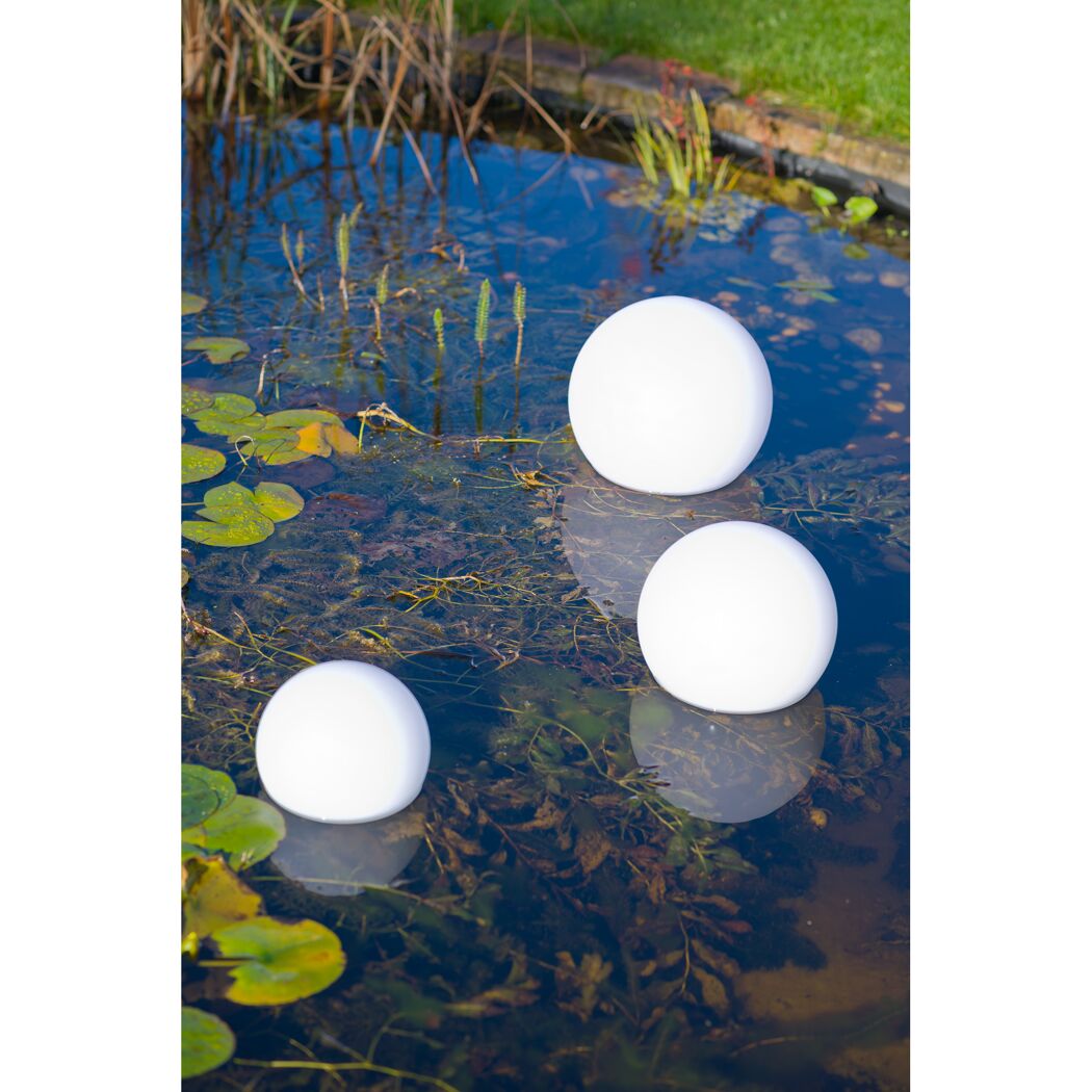 Drei weiße Kugelleuchten schwimmen auf einem Teich
