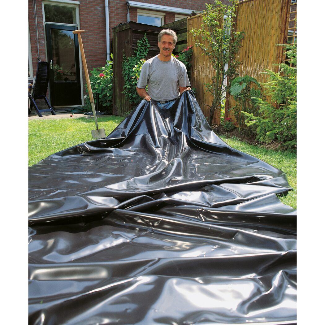 Person breitet schwarze Teichfolie im Garten aus.