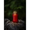 Rote Glas-Grabkerze mit brennender Flamme auf Felsen.