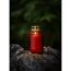 Rote Glas-Grabkerze mit brennender Flamme auf Felsen.