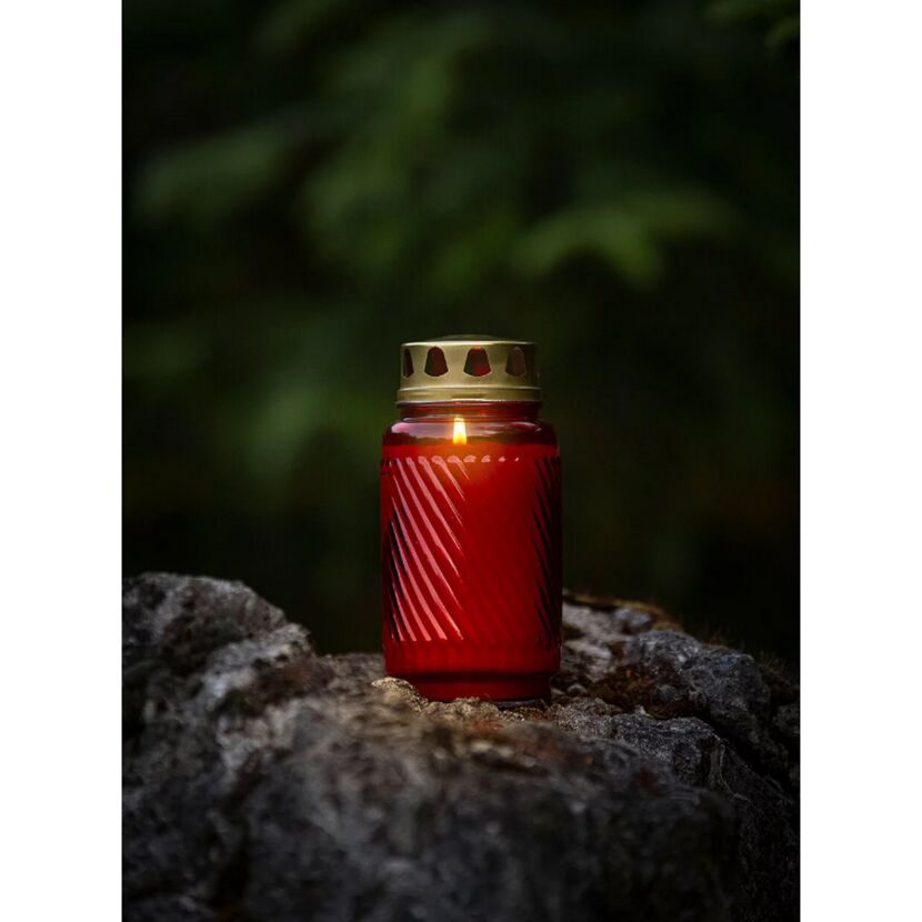 Rote Glas-Grabkerze mit brennender Flamme auf Felsen.