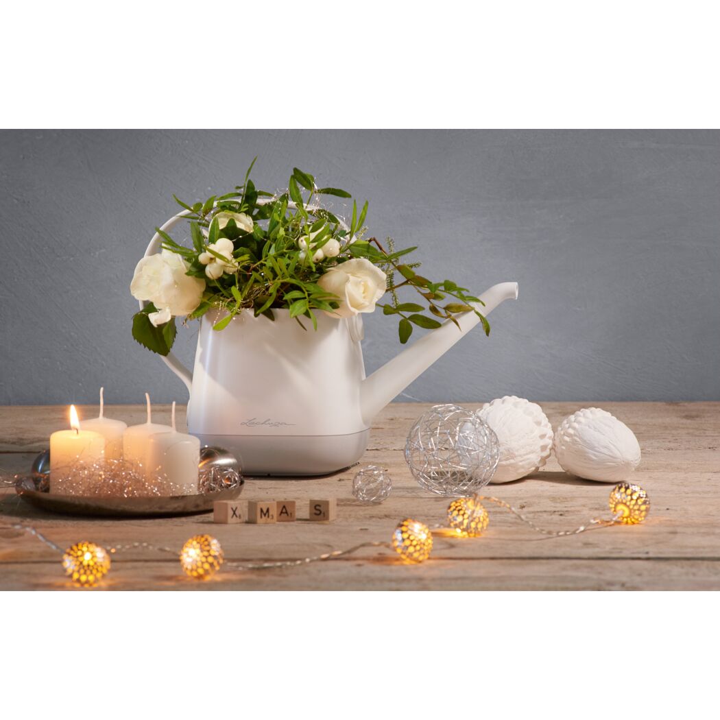 Weiße Gießkanne mit Blumen und Weihnachtsdeko