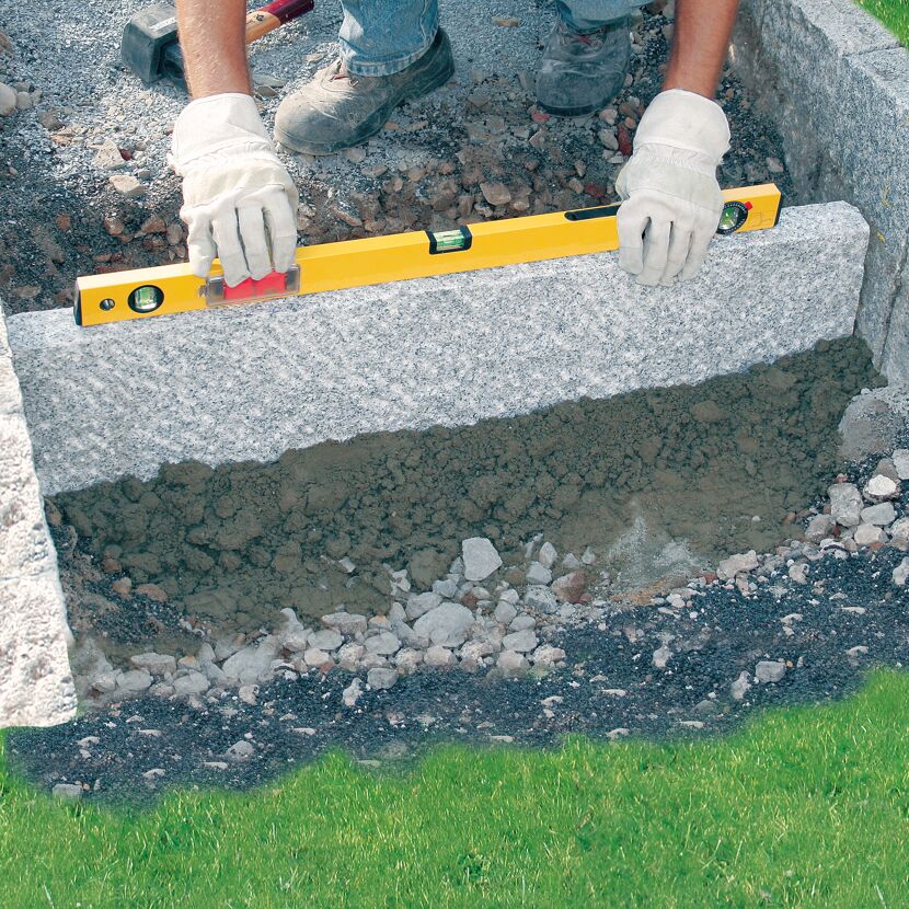 Person verwendet Wasserwaage beim Verlegen von Granitsteinen