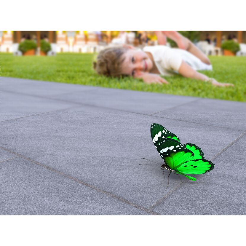 Kind liegt auf dem Rasen, ein grüner Schmetterling auf den Fliesen.