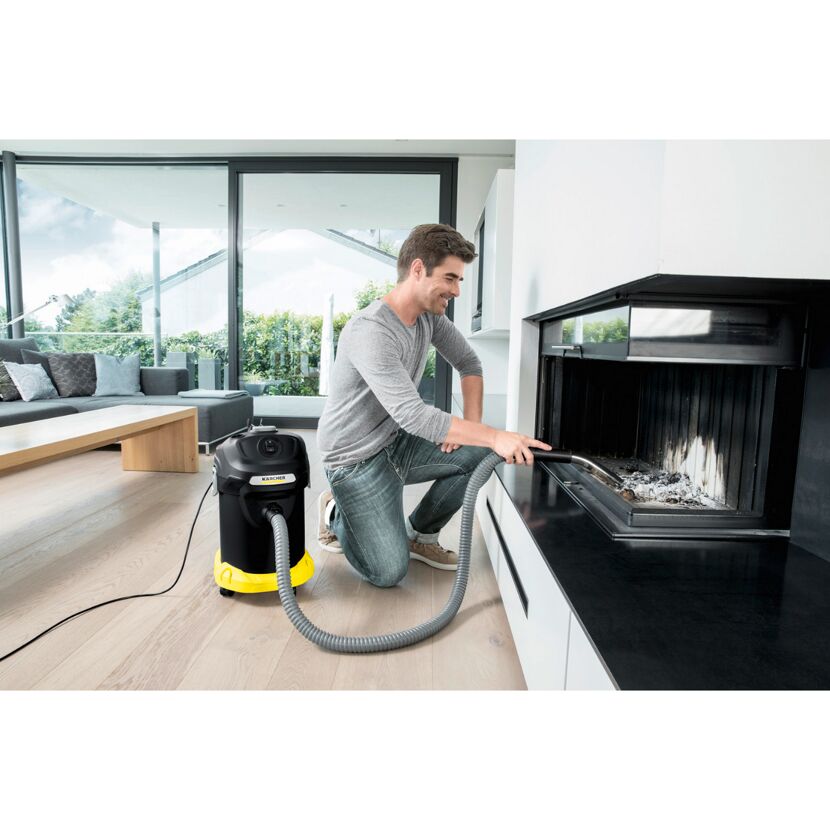 Person saugt Asche mit einem Aschesauger aus einem Kamin.