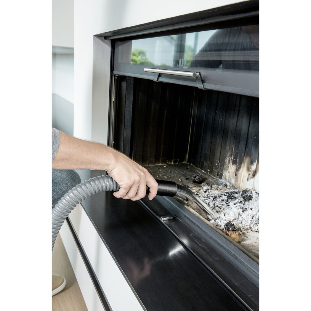 Person saugt Asche mit einem Aschesauger aus einem Kamin.