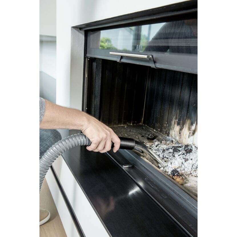 Person saugt Asche mit einem Aschesauger aus einem Kamin.