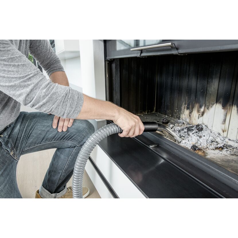 Person saugt Asche mit einem Aschesauger aus einem Kamin.