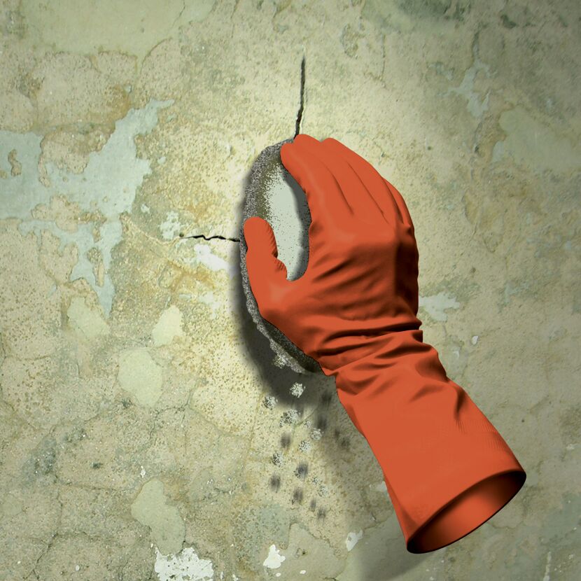 Eine Person trägt einen orangefarbenen Handschuh und reibt mit einem Schwamm über eine Wand.