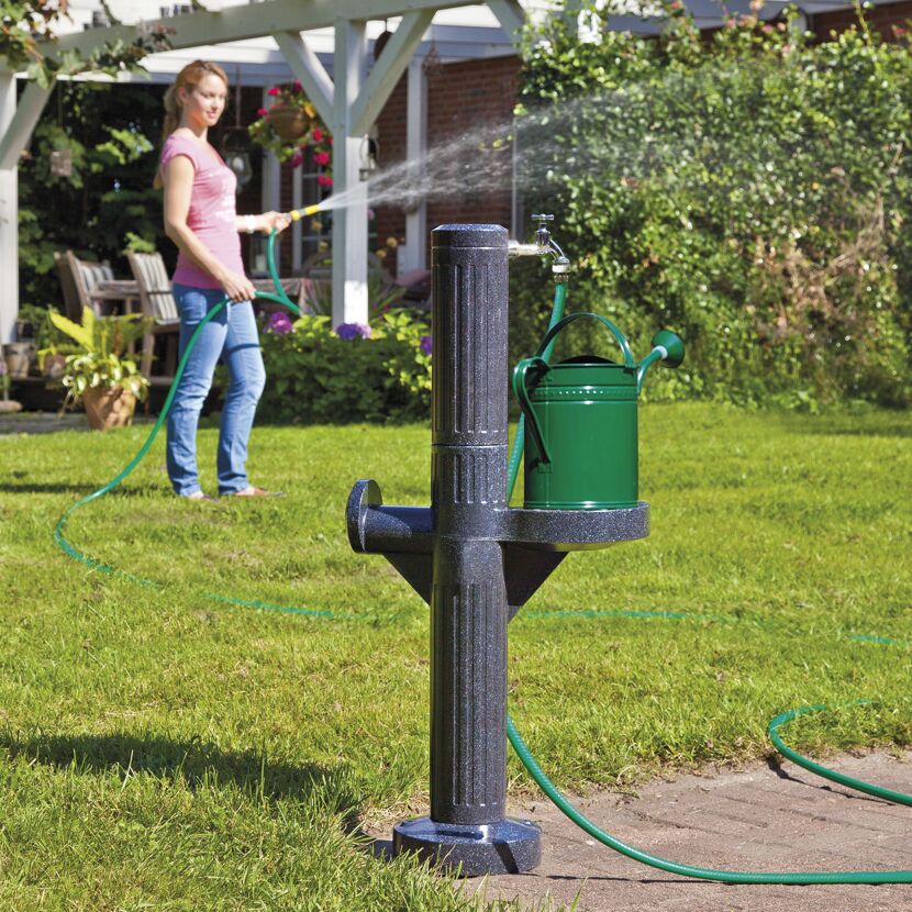 Person gießt mit Gartenschlauch eine Gießkanne.