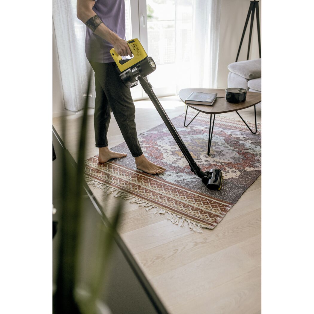 Person saugt einen Teppich mit einem Stielstaubsauger
