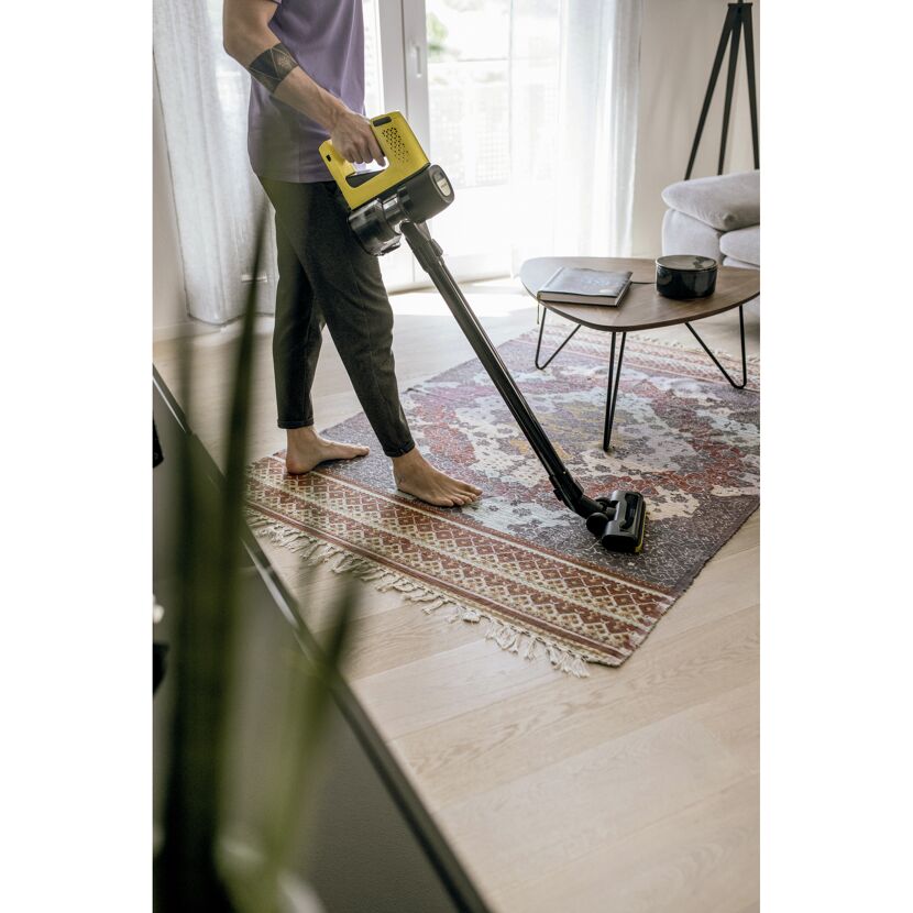 Person saugt einen Teppich mit einem Stielstaubsauger