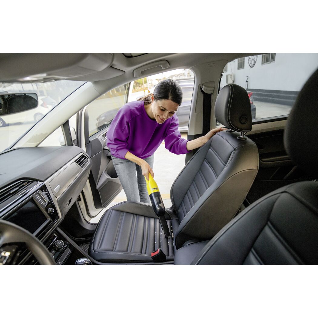 Person saugt Autositz mit Handstaubsauger