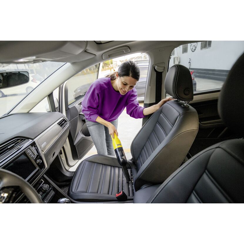 Person saugt Autositz mit Handstaubsauger