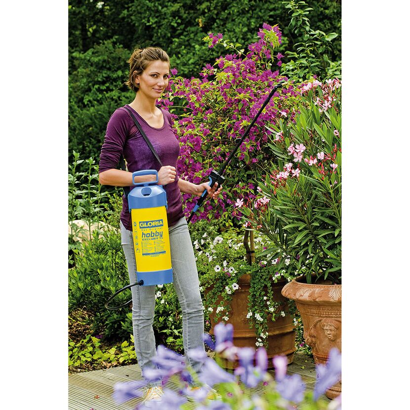Person sprüht mit Drucksprühgerät Pflanzen im Garten