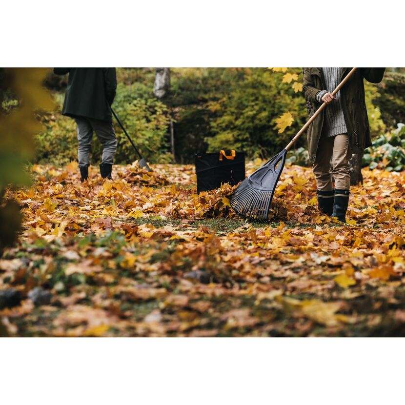Personen harken Laub im Herbst mit Laubbesen