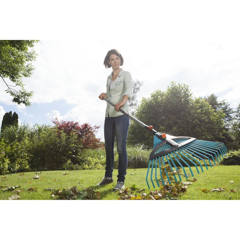 Person rechen Laub im Garten mit einem Laubbesen.
