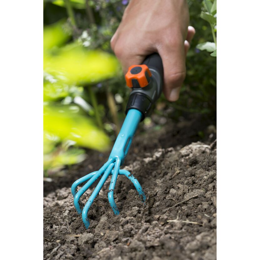 Hand harkt mit Blumenkralle den Boden