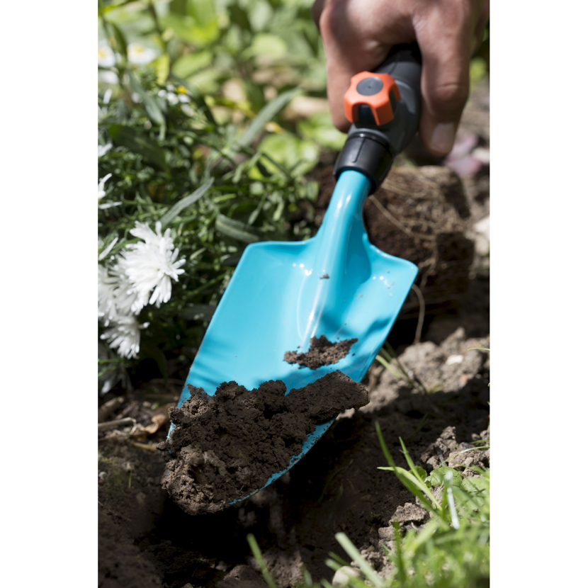 Hand hält eine blaue Blumenkelle mit Erde
