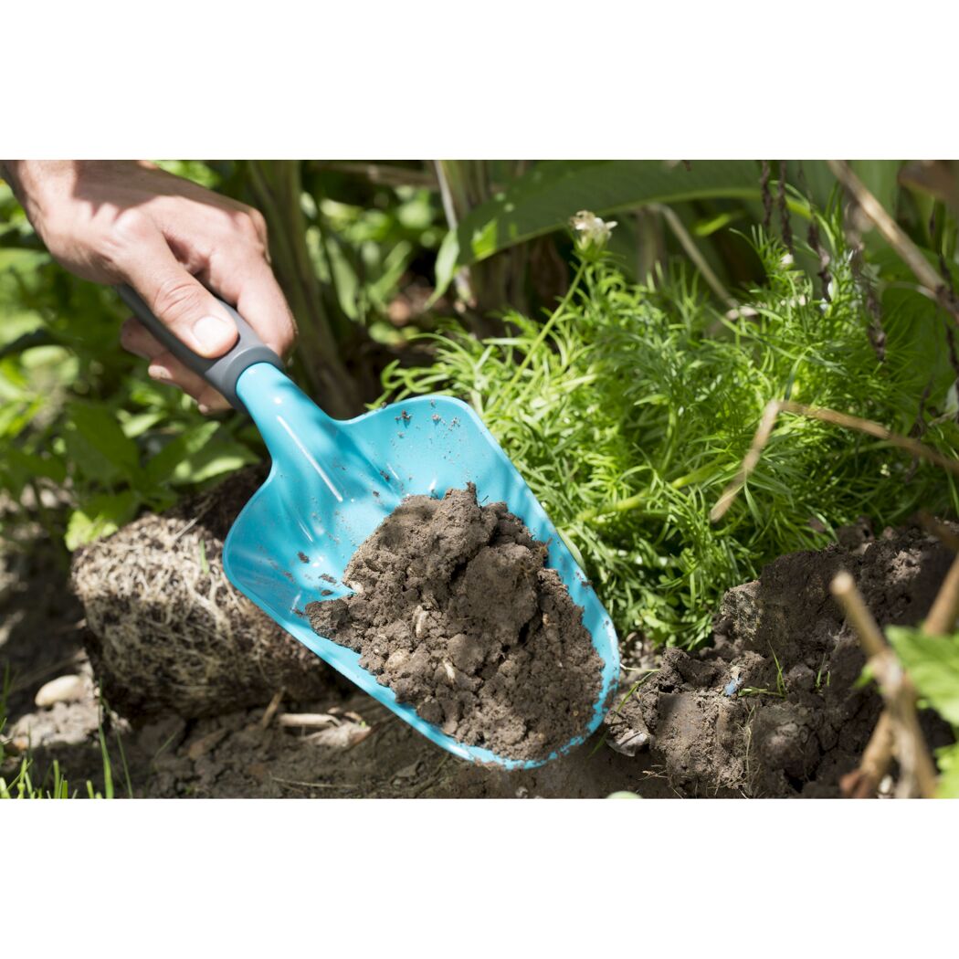 Person hält blaue Blumenkelle mit Erde