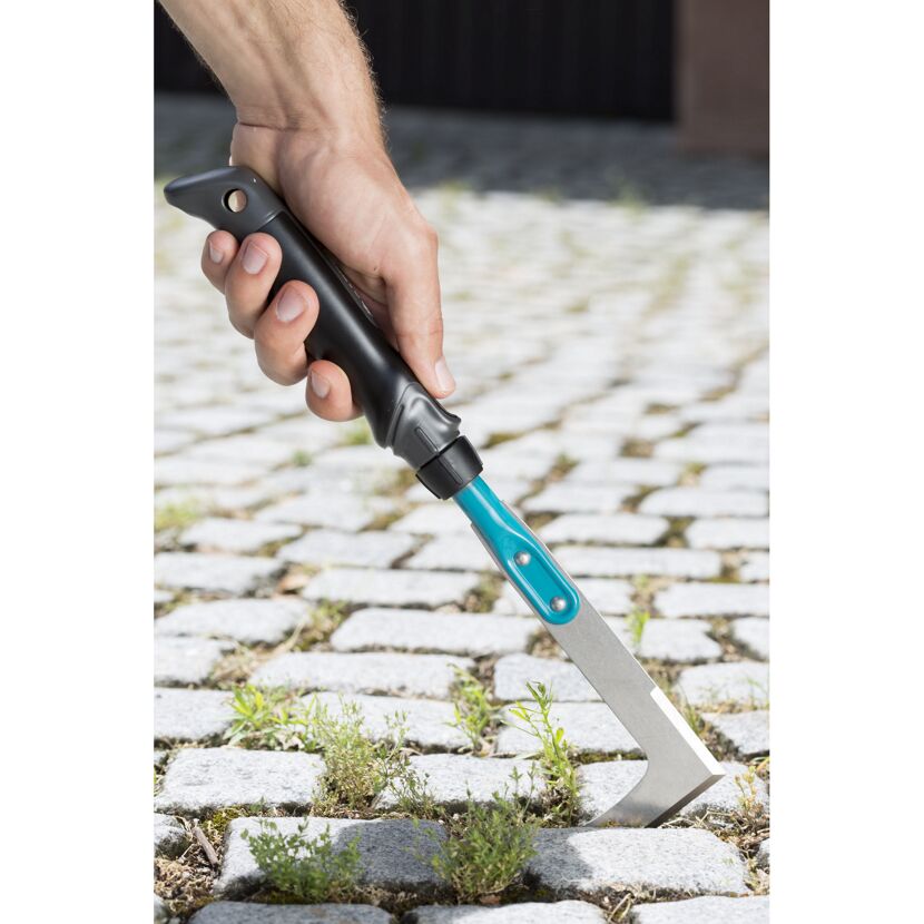 Eine Person entfernt Unkraut mit einem Fugenkratzer.