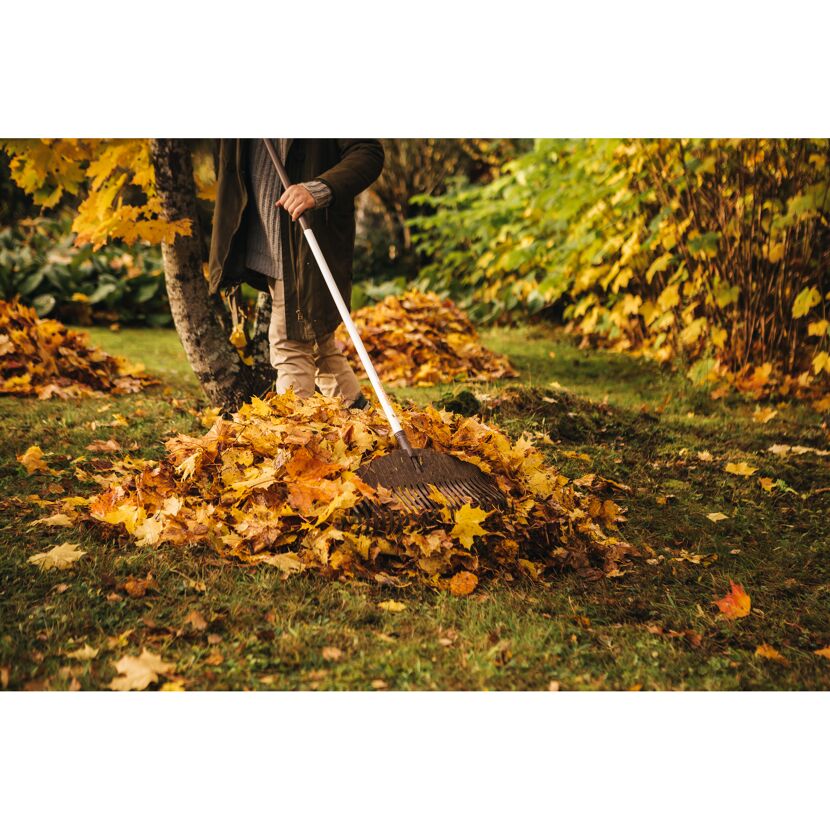 Person häuft mit Laubbesen Herbstlaub auf.
