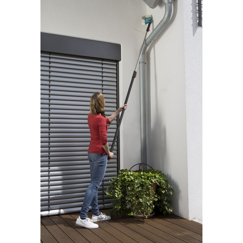 Person reinigt Hauswand mit Winkelbesen.
